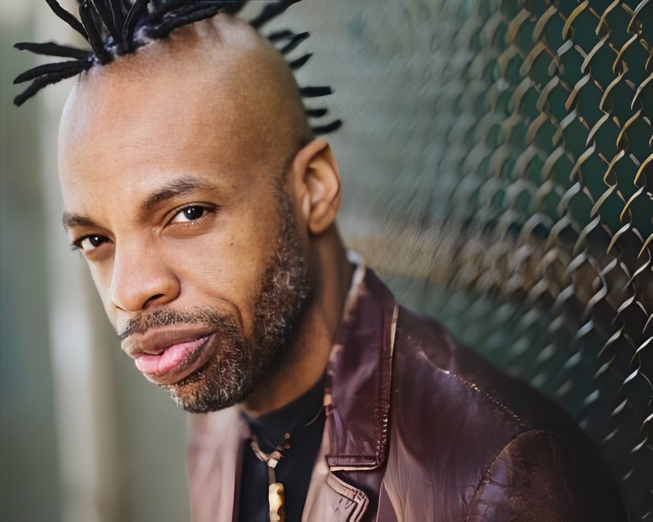 Confident man standing by a chain-link fence